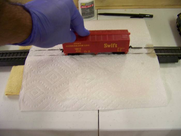 To clean the wheels on train cars, I drape a paper towel over a track segment then add a couple drops of Rail-Zip where the paper towel touches the rail head. I then place the rail car on the track and move back and forth until wheels are clean.