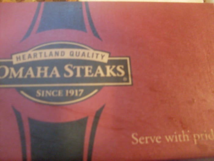 Food products from OMAHA STEAKS company are placed in sturdy and neat cardboard boxes for shipping. The boxes include black and burgundy colors & the Omaha Steaks company logo. The packaged food presentation is lovely.