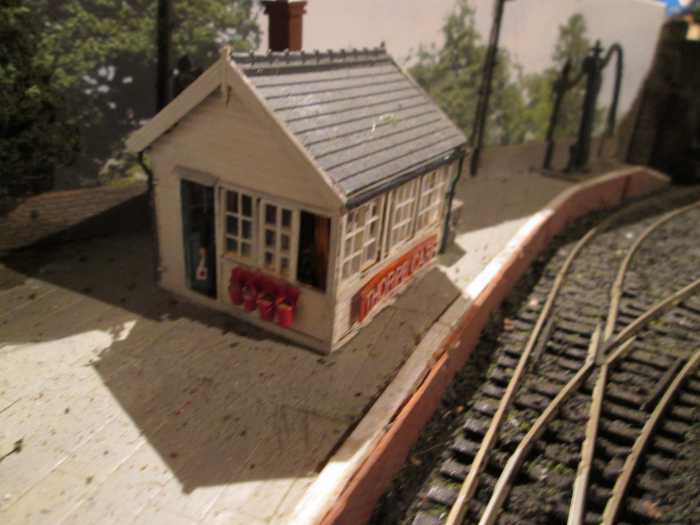 Signal cabin with open door and porter leaning in (lamp in hand) to speak to the 'bobby' ; Wills' (signalman); Interior detailing added. Wills' dressed stone wall (behind) and brick platform facing on pine framework; Mike's Models NER water crane