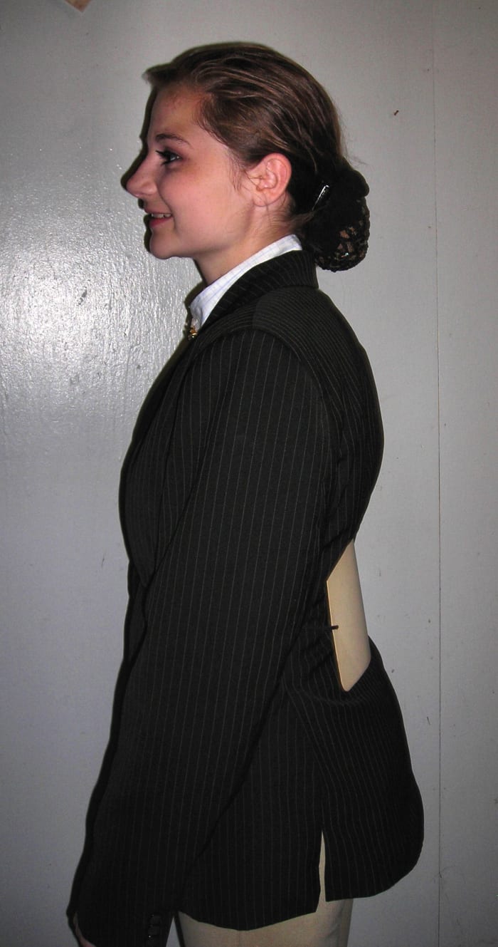 Not so perfect -- Tied too snug. Coat is puckering and the number is already starting to tuck down into the waistline of her breeches.