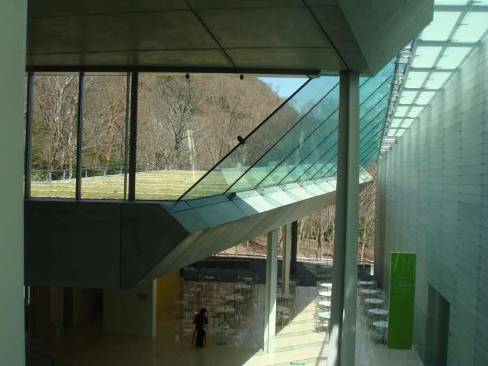 Photo taken from the ground level, captures one floor down featuring the cafe, and the roof of the structure, all grassy, is clearly visible through the glass.