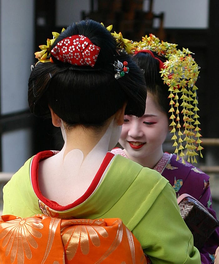 Geisha's kimonos are known for the neckline in the back which shows off white marks on the nape of the neck. The obi in a geisha's kimono is wide and high. They wear a headdress, usually of synthetic hair, with elaborate kanzashi, or hair ornaments.