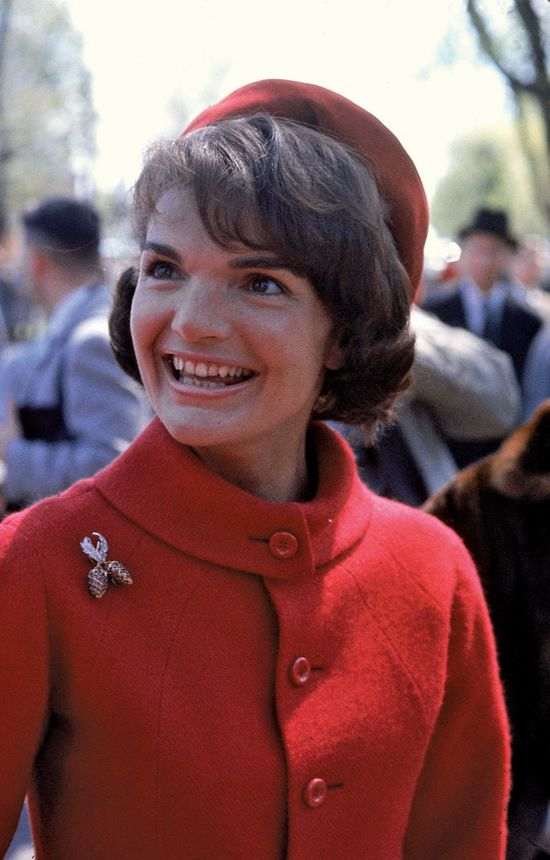 Jackie Kenned in a red suit with matching hat and wearing on her right shoulder the ruby brooch