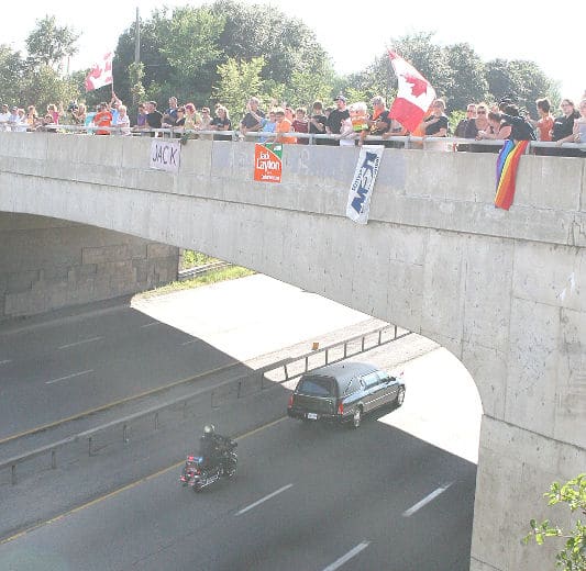 People wave Canadian flags and signs from an overpass as the hearse carrying Jack Layton's body passes along HWY 401 at Kingston, Ont., Thursday, Aug. 25, 2011.