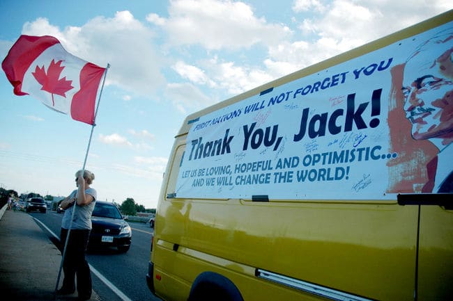 A Canadian flag is waved in Trenton, Ont., while waiting for Jack Layton's funeral motorcade to pass Thursday, Aug. 25, 2011.