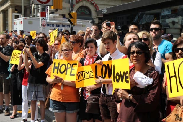 Mourners along the procession route carry signs that read "Hope," "Optimism" and "Love," invoking Layton's farewell letter.