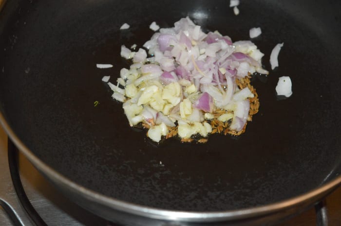 Step three: Heat oil in a deep-bottomed pan. Throw in cumin seeds. Let them crackle. Add chopped garlic and onions. Saute until they become pinkish.