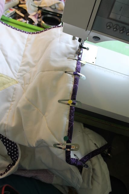 Attaching bias binding to the edge of a quilt to create a bound hem. I like the use of hairclips to hold the binding on.