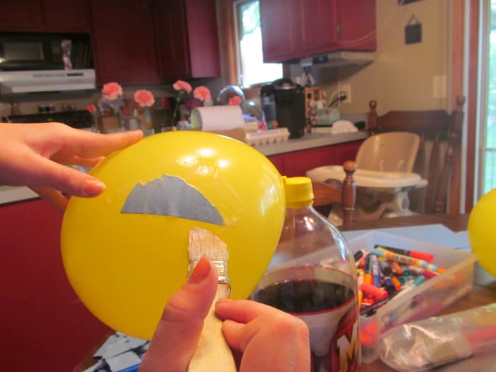 Begin to attach your ripped paper to the balloon. It work best to lay the paper on the balloon and then hold the balloon with one hand and paint the glue on top of the paper with the other hand. (That is why you need something heavy to anchor it.)