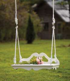 romantic Victorian swing in white with graceful wooden curves with roping and pink roses resting gracefully on the seat