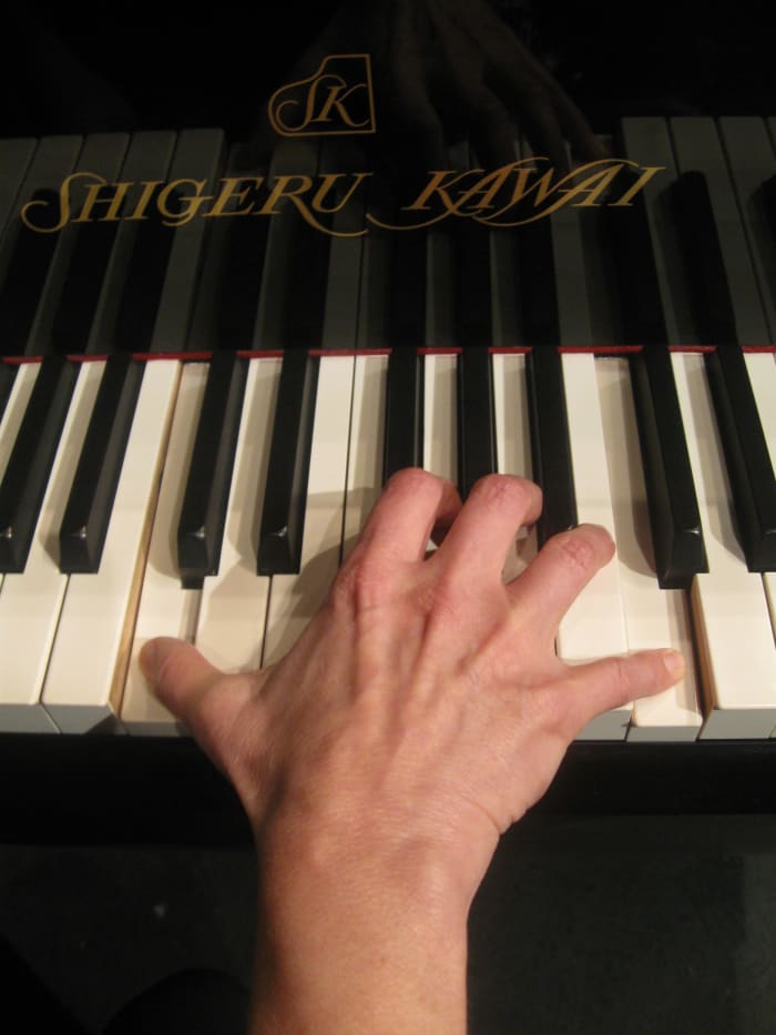 Woman's hand playing an octave on a full size piano. Notice the strain across the knuckles due to the stretching required to reach the notes.