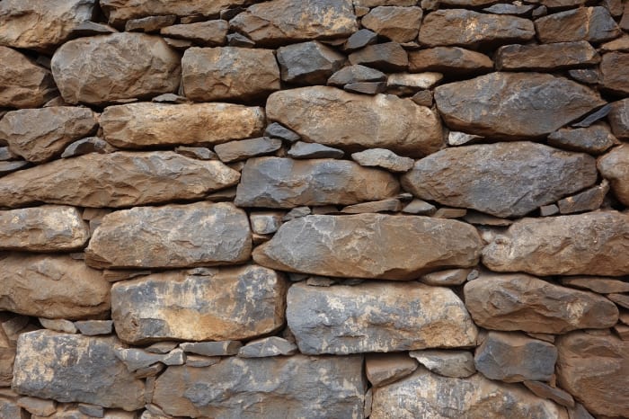 A dry-built stone wall is reminiscent of the layers of earth revealed in a road cut through a mountain, except that in a mountain cut, the layers extend for hundreds of feet or even miles