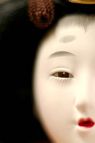 Detail of Gofun doll face shows individual expression with traditional makeup. Tiny brushes are used to create individual hairs of eyelashes and brows.