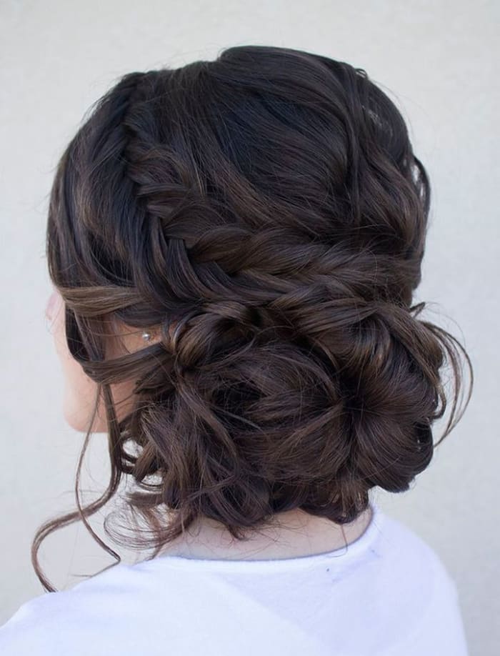beautifully arranged dark brown to black hair in a low bun resting at the nape. Braid snakes around the hairdo