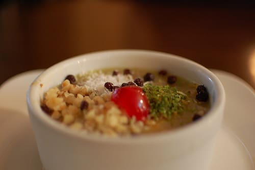 A small bowl of asure topped with grated pistachios, nuts, raisins & other currants.