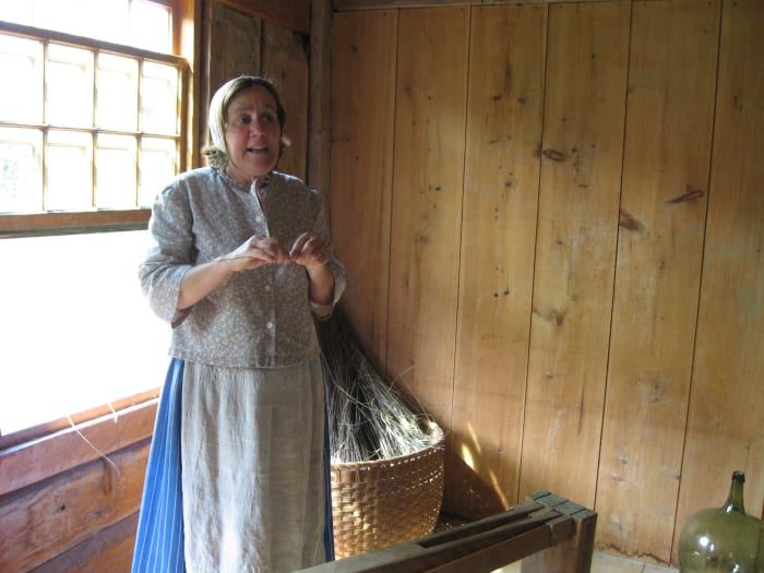 The same docent explains to visitors how they make the fabric. In the basket behind her, you see the flax waiting to be made into fiber for weaving.