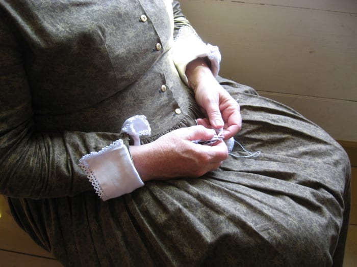 Here's a woman is making lace. You can see examples of it on the cuffs of her dress. This dress appears more formal than that worn by women in the more humble homes. The dress fabric is probably store-bought.