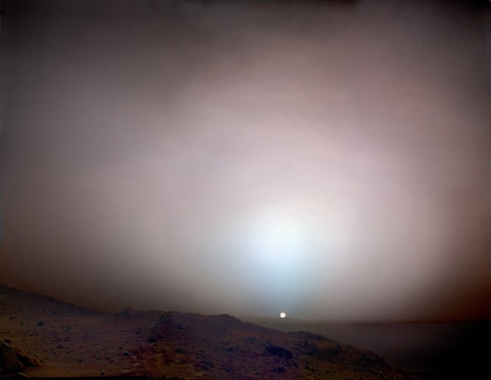 Sunset on Mars. Appearing only about two-thirds the size it does from Earth, the Sun sets behind the 50-mile-distant rim of Gusev Crater. The blue glow is caused by light-scattering dust suspended in the atmosphere. Mosaic composite photograph. Taken