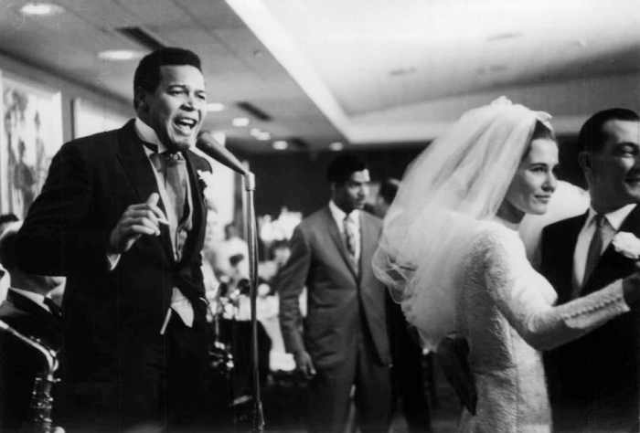 Photo of Chubby Checker singing at his wedding reception while his new bride, Catharina Lodders, dances with a guest. Chubby Checker was married in Philadelphia April 12, 1964.