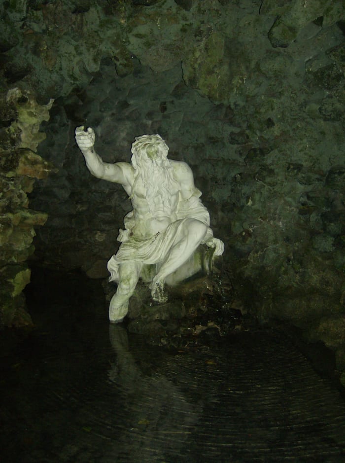 A statue sitting on a rock Inside one of the water grottos. These grottos are a great place to sit for a few minutes and cool off on a hot day.