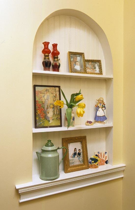 decorative alcove with shelves topped with a graceful arch on a plaster wall with bead board as the background