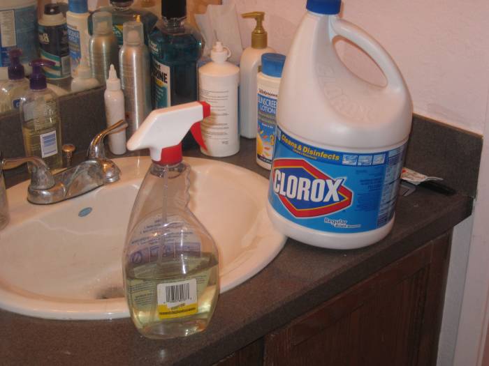 Filling a spray bottle with mixture of bleach and water to spray behind wall to prevent growth of mold.