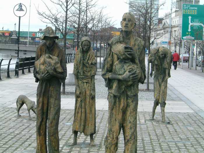 Customs House Quays, Dublin. Painfully thin sculptural figures, by artist Rowan Gillespie, stand as if walking towards the emigration ships on the Dublin Quayside.