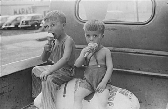 "Farm boys eating ice-cream cones. Washington, Indiana" 1941. Two boys seated on sacks in back of pickup-truck eating ice-cream.