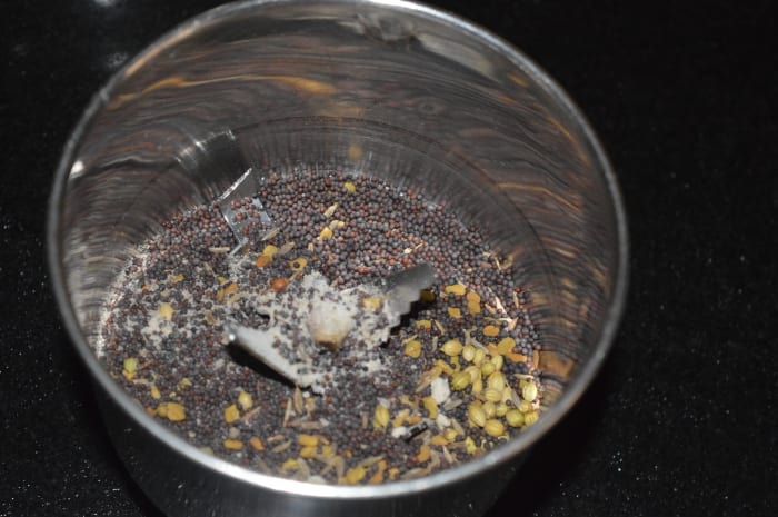 Step two: Heat the ingredients for making garlic pickle as per instructions. Add warmed mustard seeds, fenugreek seeds, cumin seeds, coriander seeds, and hing powder to a mixer. Grind them to get a fine powder.