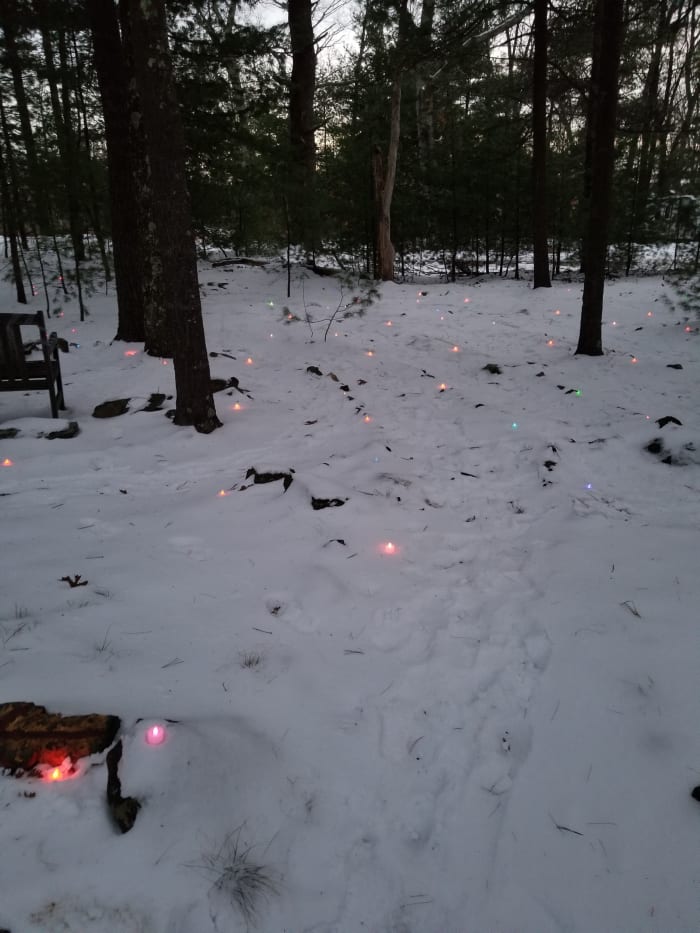 Footprints on the snowy wooded labyrinth path lit with rainbow lights for the Winter Solstice in New England. Dusk is a magical time to walk a labyrinth. It is the time of transition between afternoon and evening.