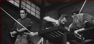 Red Beard and a colleague operate on a patient as Yasumoto struggles to keep her still on the operating bed.