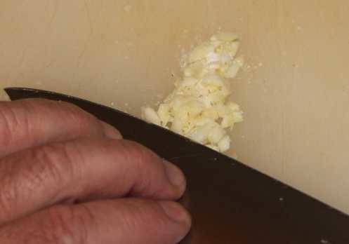 Repeatedly draw edge of your knife over the garlic, while pressing down with your fingers, to mash the garlic into a paste.