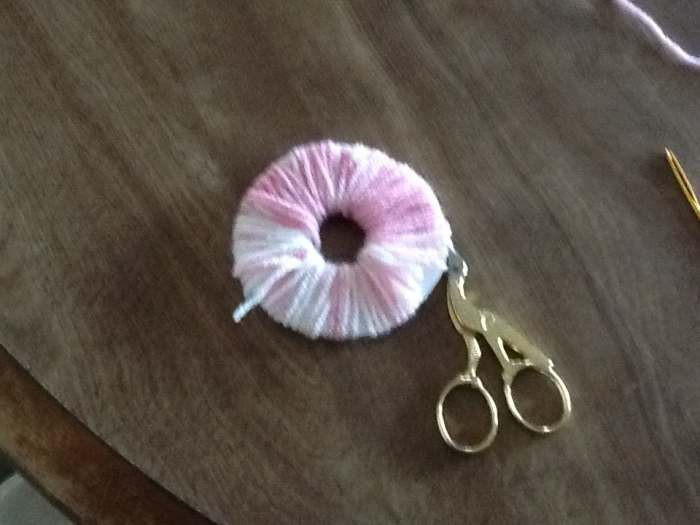 With scissors cut the yarn carefully around the out side edge. Your scissor blade should go between the two pieces of cardboard.