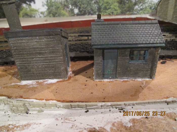 The two huts complete with chimney stacks, guttering and downpipes, painted, at the lineside, fixed down on white plastic bases, ready for scenic work to be undertaken around them. The choice is broad, what would you make of their surroundings?