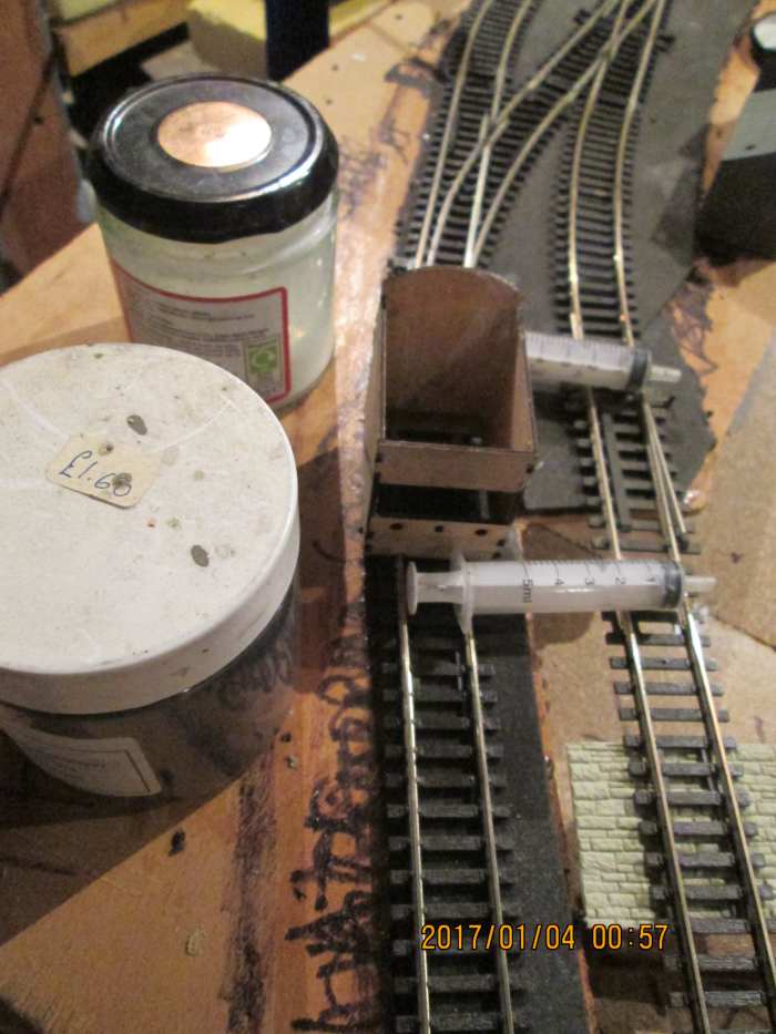 The tools for the ballasting job: large syringes suitable for pushing through dilated PVA/wood glue solution + washing-up liquid, jar of ballast (ash) and Poppy's Woodtech box with its 'chute' and lateral slot to allow an even flow of ballast