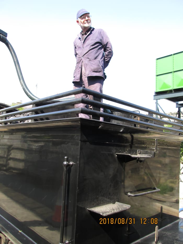 Driver Terry Newman looks along the platform from the back of the tender as 65894 receives water from the new crane at Leyburn