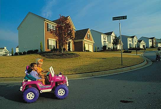 Two girls enjoy the safe and quiet serenity of their neighborhood- taking their Barbie Jeep out for a spin.