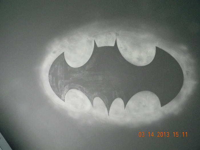 This is the glow in the dark Bat Symbol on the ceiling of the Batman themed bedroom. The outlying oval glows around the black symbol giving the illusion of an actual light being shown on the clouds above. It was produced with Krylon Glowz spray.