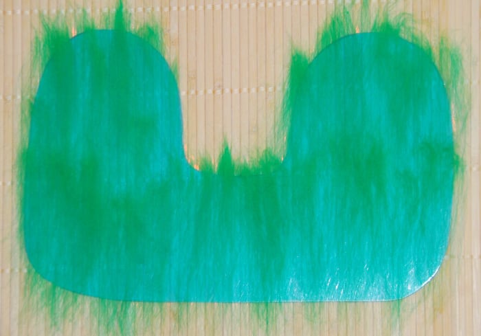 Template shown on a bamboo mat with a thin layer of green fibers placed down on it.