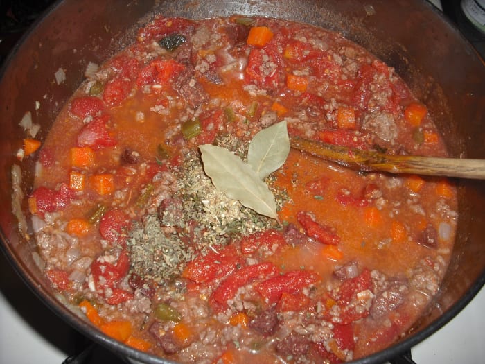 Add the whole tomatoes (crushed with your hands), tomato paste, parsley, basil, oregano and bay leaves. Stir well.