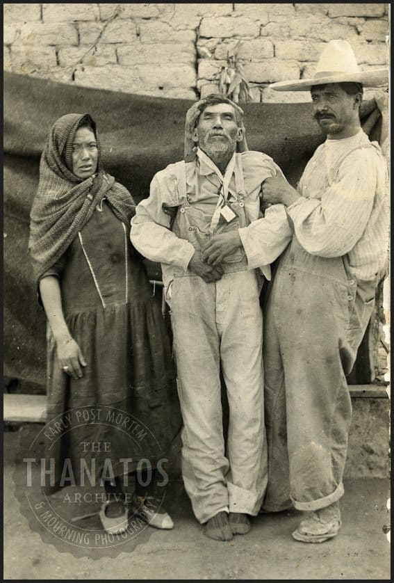 An early post mortem photo showing three people holding up the dead body. The third is holding the head.