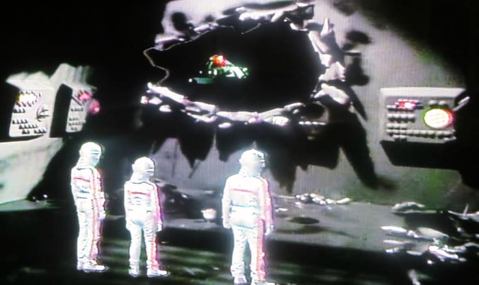 Oro's Ship taking off from the Starlost and Heading back to his home world. Devon, Rachel and Garth are in their spacesuits looking out of the damaged hole Oro made to the Ark when he crashed into it.
