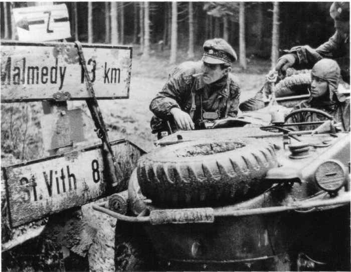 Checking a highway sign at an Ardennes crossroads, an SS soldier from the 1st SS Panzer Division in an amphibious vehicle confirms a path to advance.