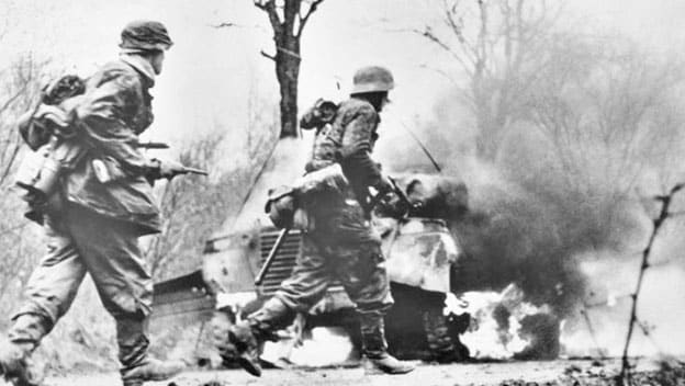 German troops advancing past abandoned American equipment early in the Battle of the Bulge.