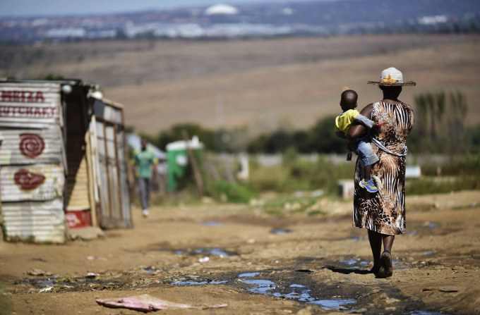 A woman carries her child as she walks alongside a line of shacks in the impoverished township of Diepsloot on the outskirts of Centurion, South Africa, on April 24.