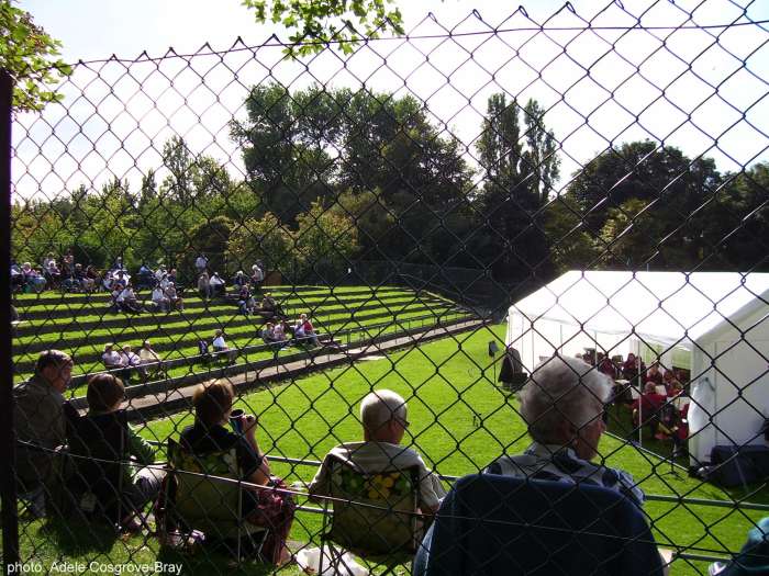 On the sunny grass tennis courts near the rose gardens, people sit to enjoy the free brass band concert organised by the Friends of Ashton Park.