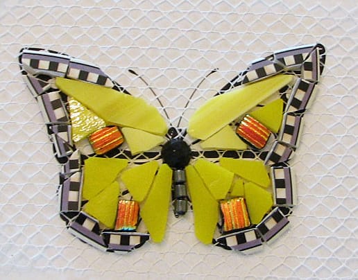Edged in plate rim. Yellow stained glass, black faceted bead cut in half and hematite bead body. Orange dichroic glass accents. Will be grouted with black grout.