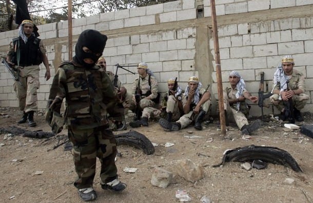 A photograph taken in Palestine of a young Arab boy as he stands in front of Palestinian Fatah Terrorists wearing camouflage and a black ski-mask