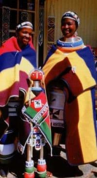 Ndebele Women and clad in their traditional Blanket and colors and standing next to their 'tall' doll