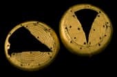 These two gold circular ornaments with double rows of incised chevron decoration resemble the top of the gold sceptre embossed with half-moon shaped decorations. the three dimensonal shaping was avhived by folding creasing and pleating the gold sheet